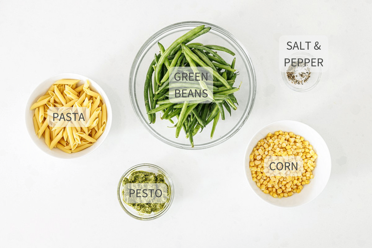 Labeled ingredients for pesto pasta salad against a white background.