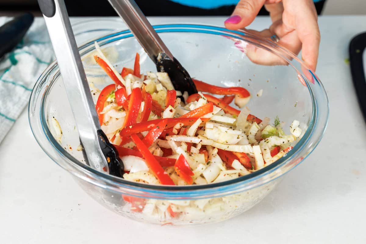 Tossing sliced veggies in a bowl in olive oil and seasoning.