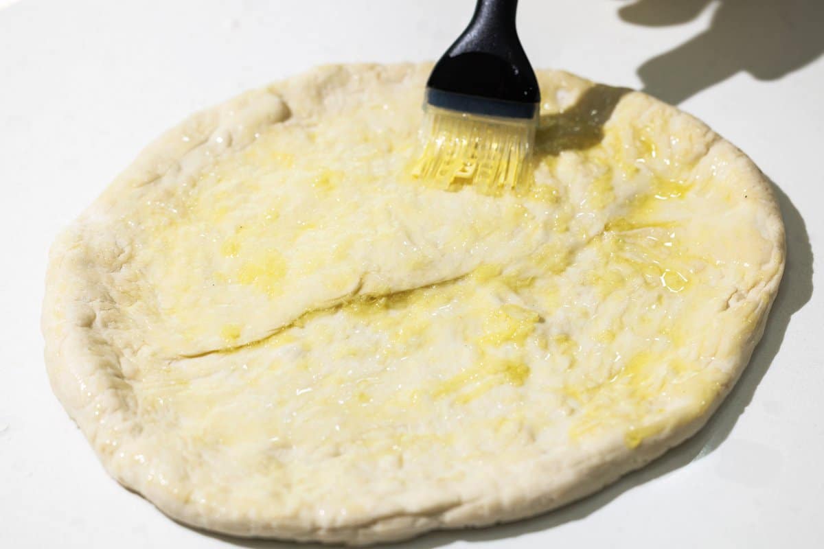 Brushing pizza dough with olive oil.