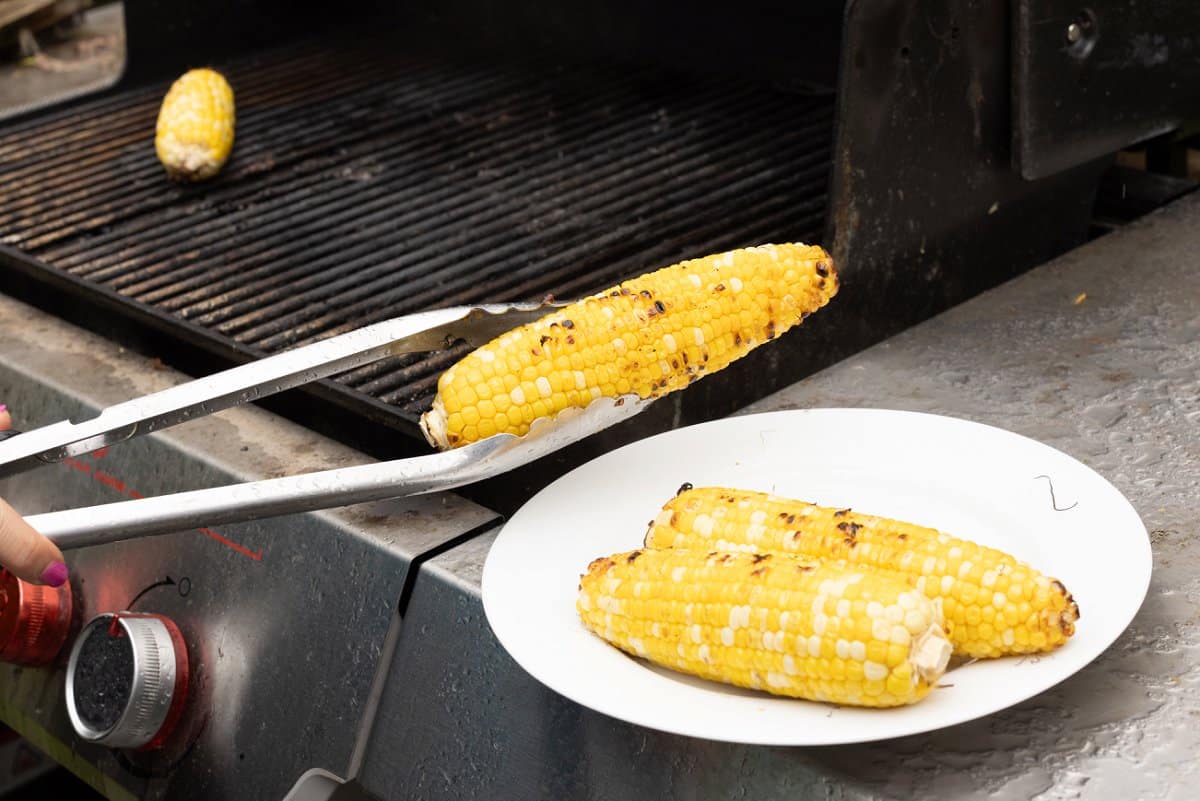 Picking up corn cobs off of grill with tongs.
