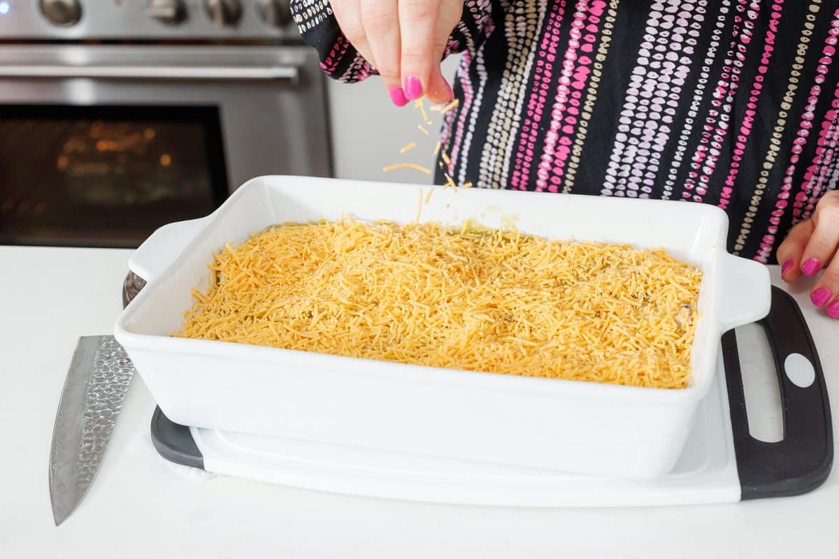 Sprinkling cheddar cheese over the top of finished Mexican lasagna.
