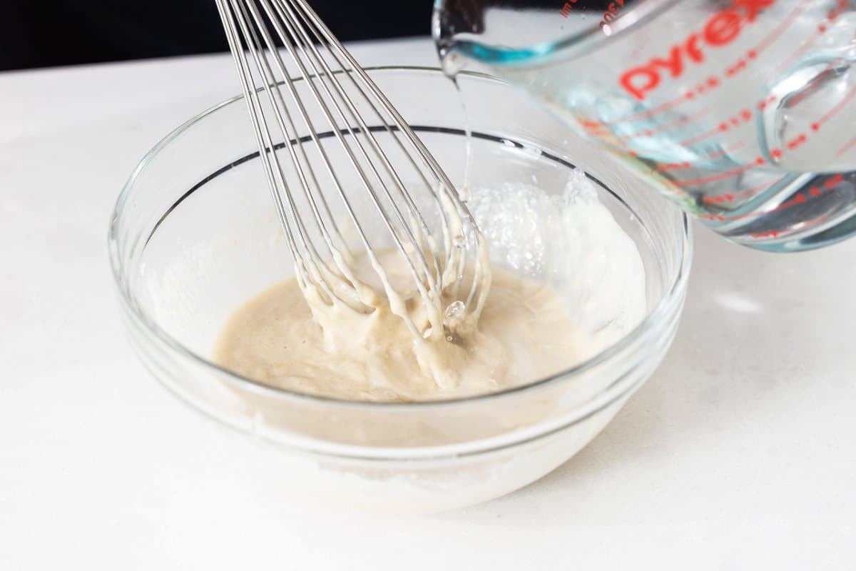Whisking tahini sauce in a large bowl.