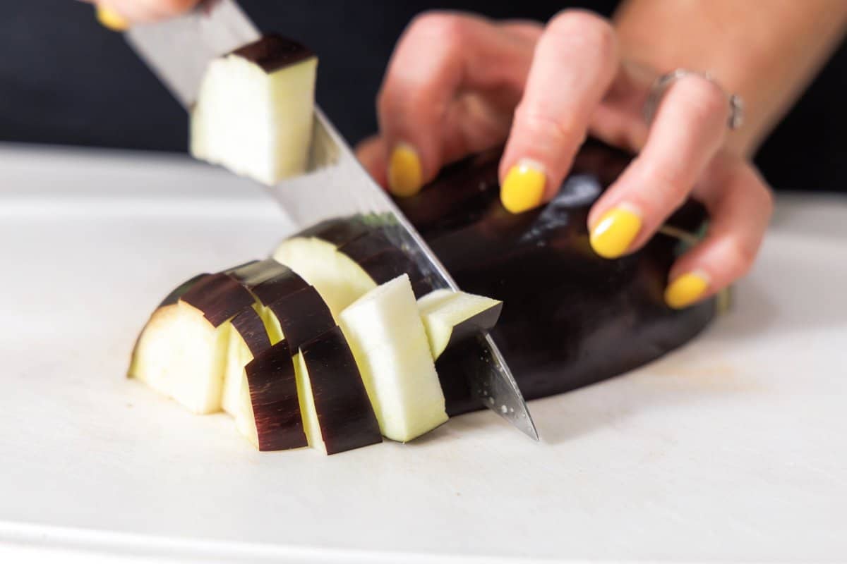 Liz cutting an eggplant into small chunks on a cutting board.