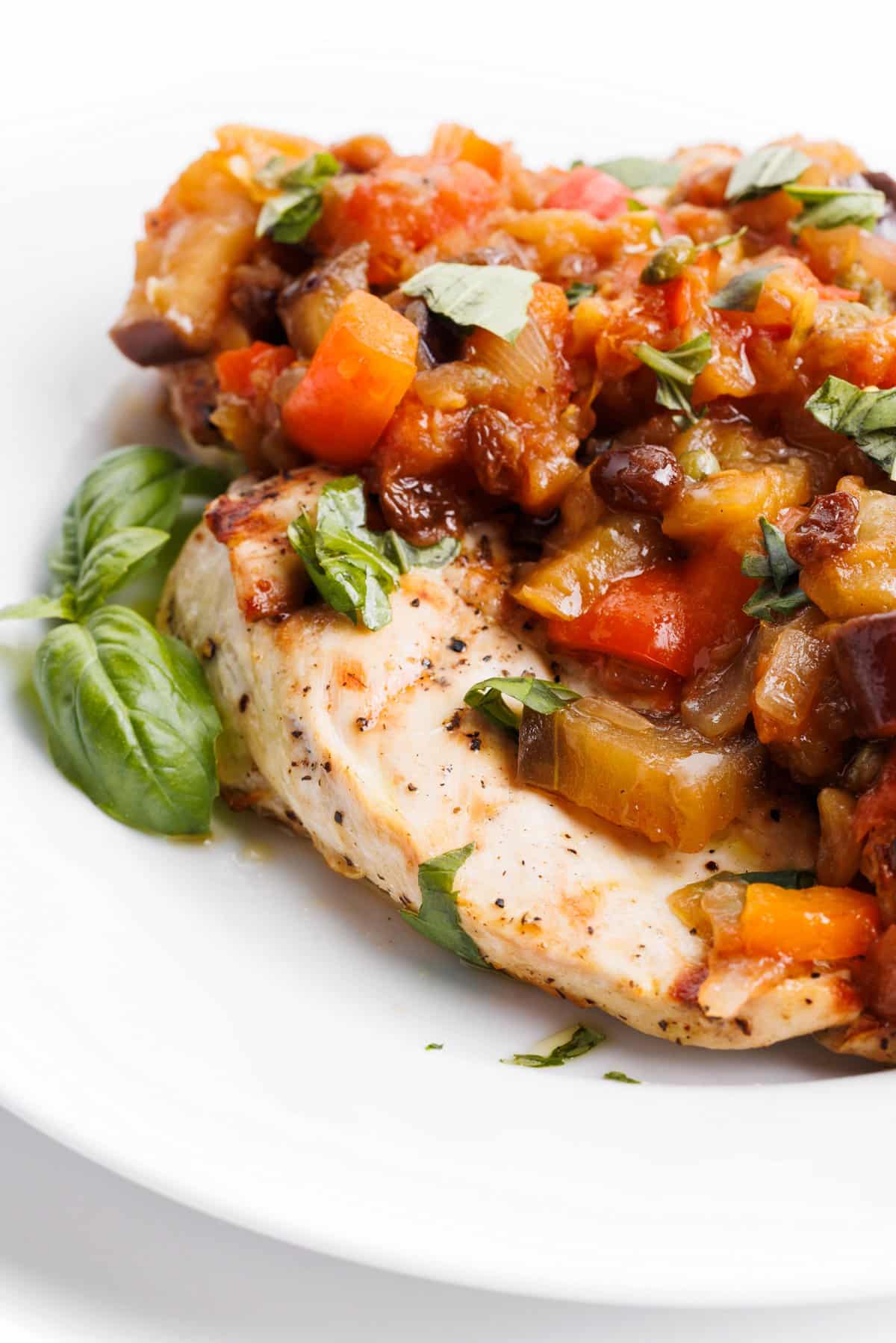 Close view of the side of a grilled chicken breast covered with eggplant caponata.