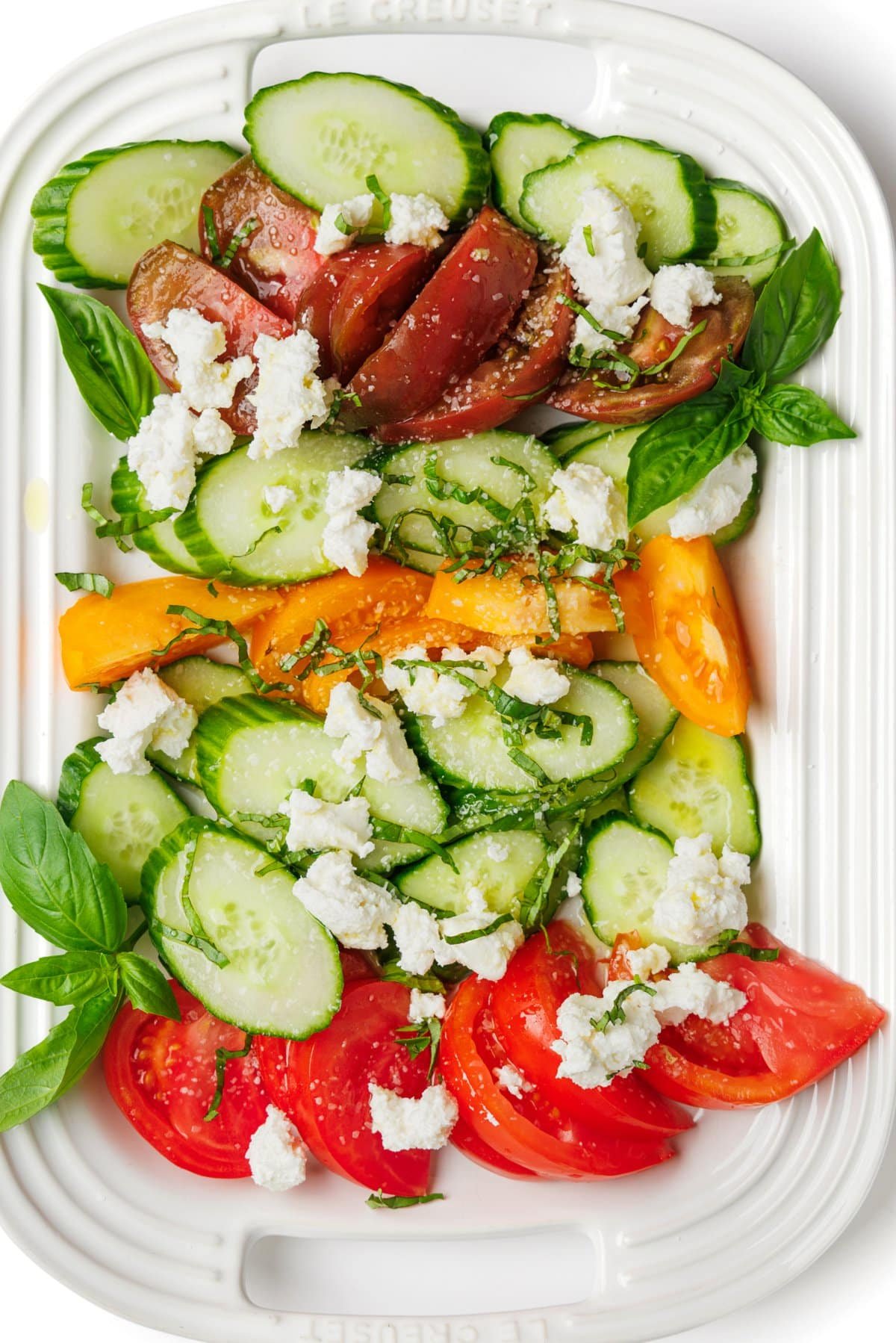 Heirloom tomato and cucumber salad with goat cheese arranged on a platter.