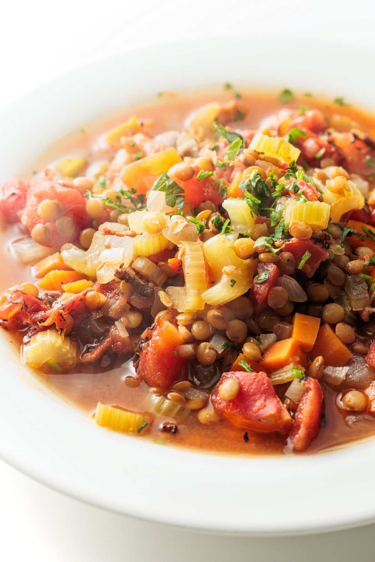 Slow cooker lentil soup with bacon garnished with fresh herbs.