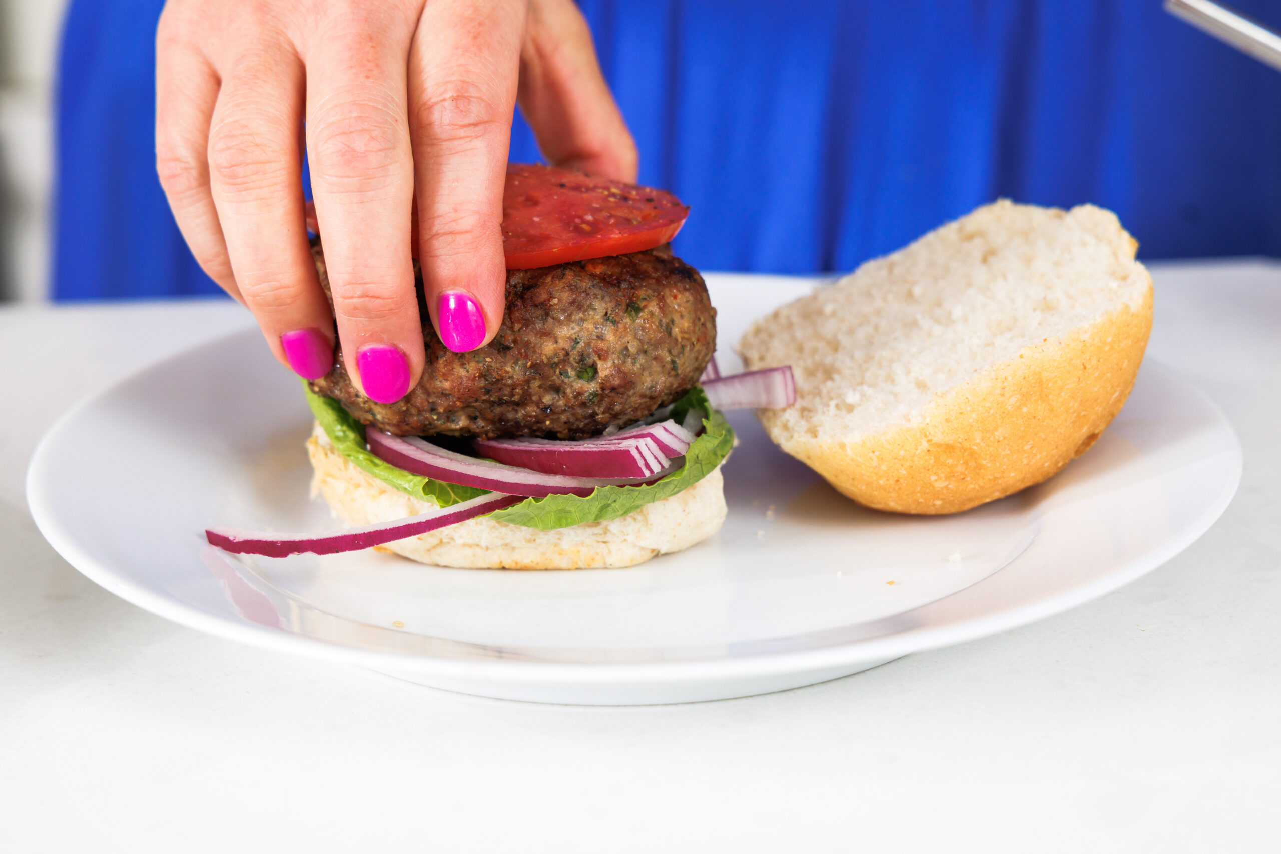 Assembling Greek lamb burger on a bun with lettuce and red onion.
