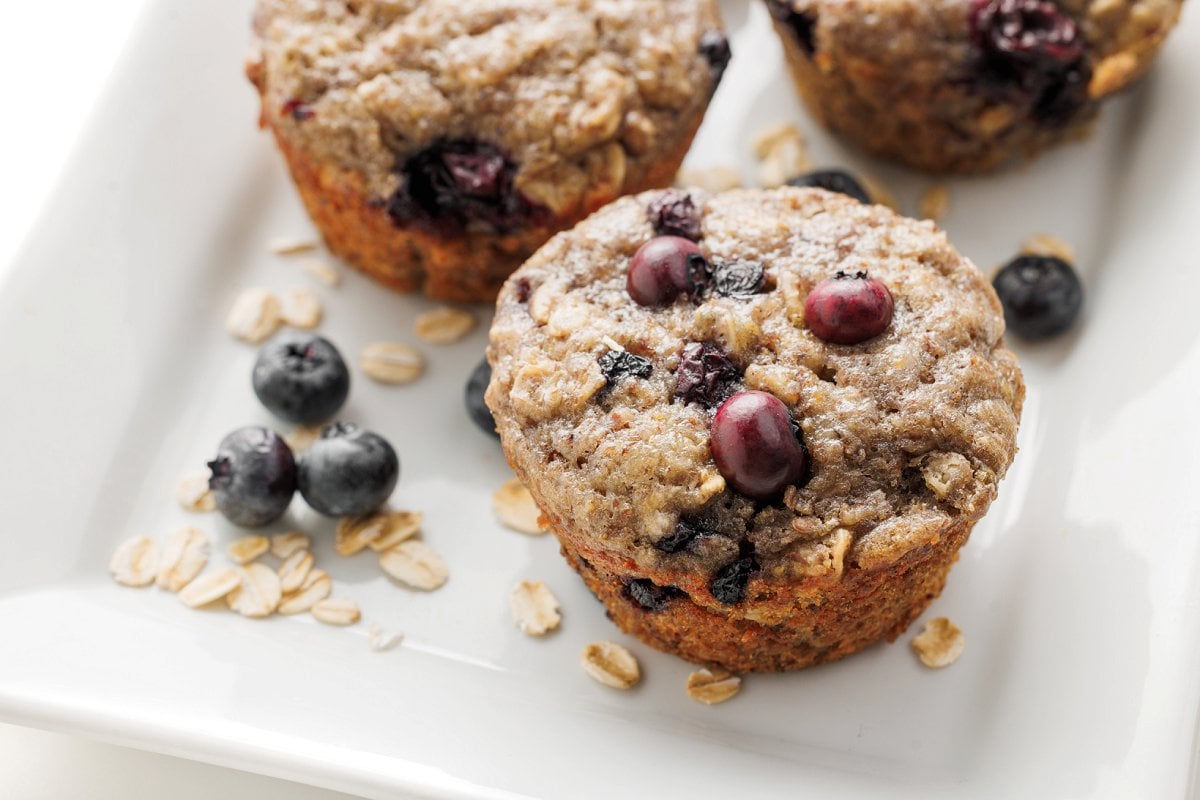 Blueberry banana flaxseed muffins on a square plate with loose oats and blueberries.