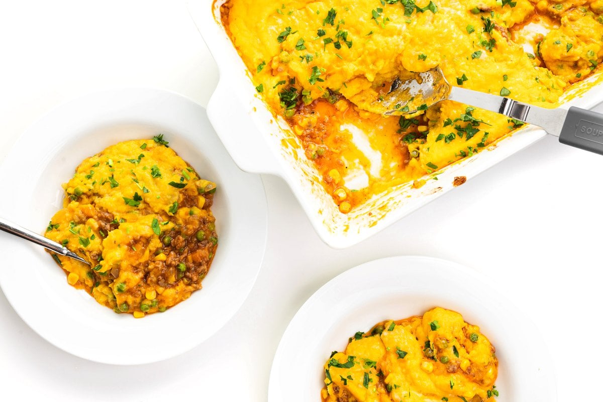 Baking dish of healthier shepherd's pie with butternut squash next to two plates fill with slices of the shepherd's pie.