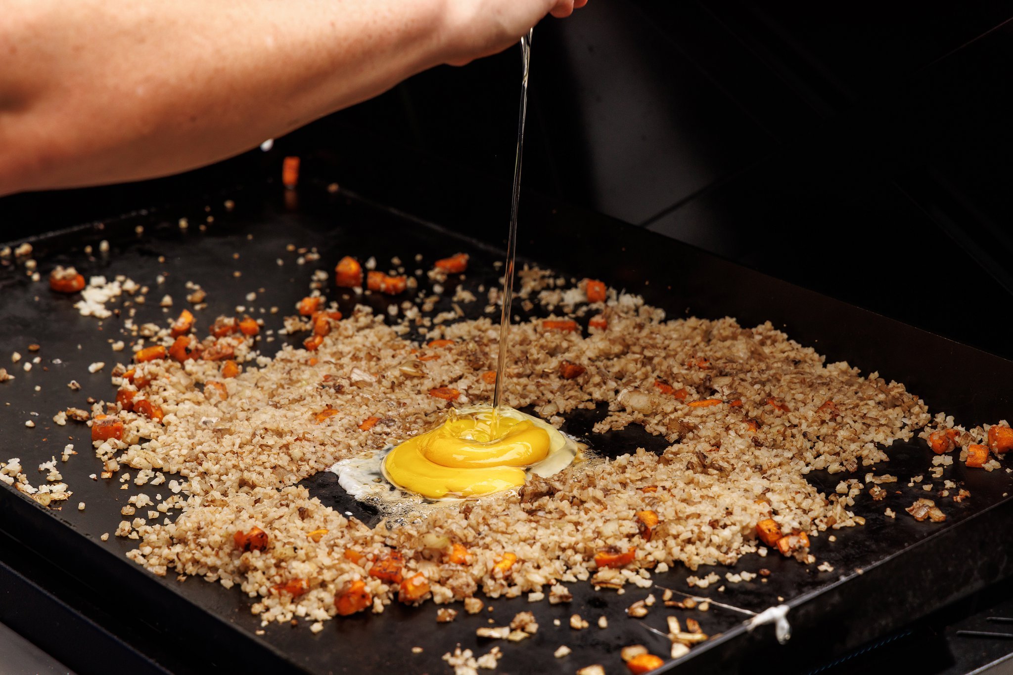 Cracking an egg into the middle of cauliflower fried rice on griddle.