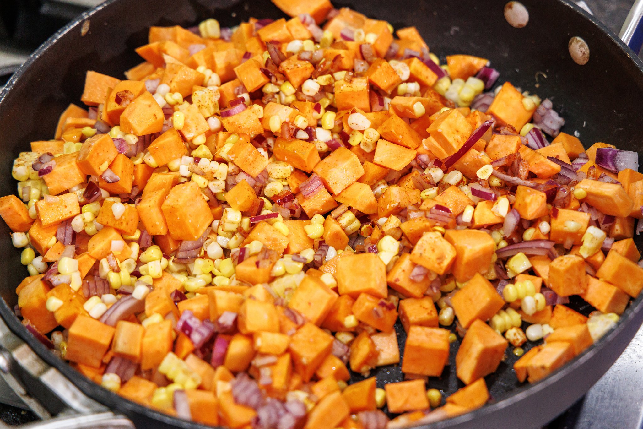 Cooking sweet potato succotash in skillet.