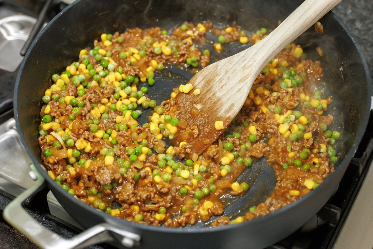 Frozen veggies added to ground lamb mix in skillet.