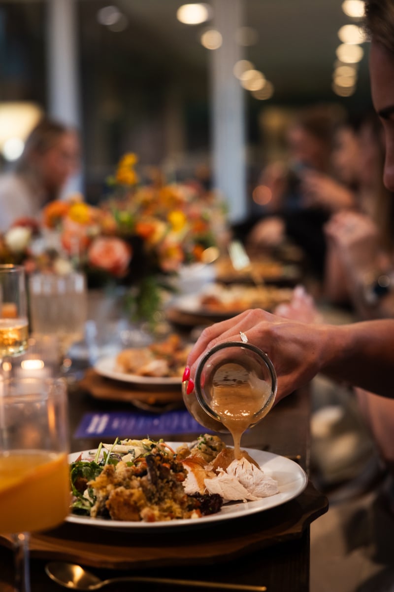 Pouring gravy from a jar over turkey, mashed potatoes, and stuffing on a plate.