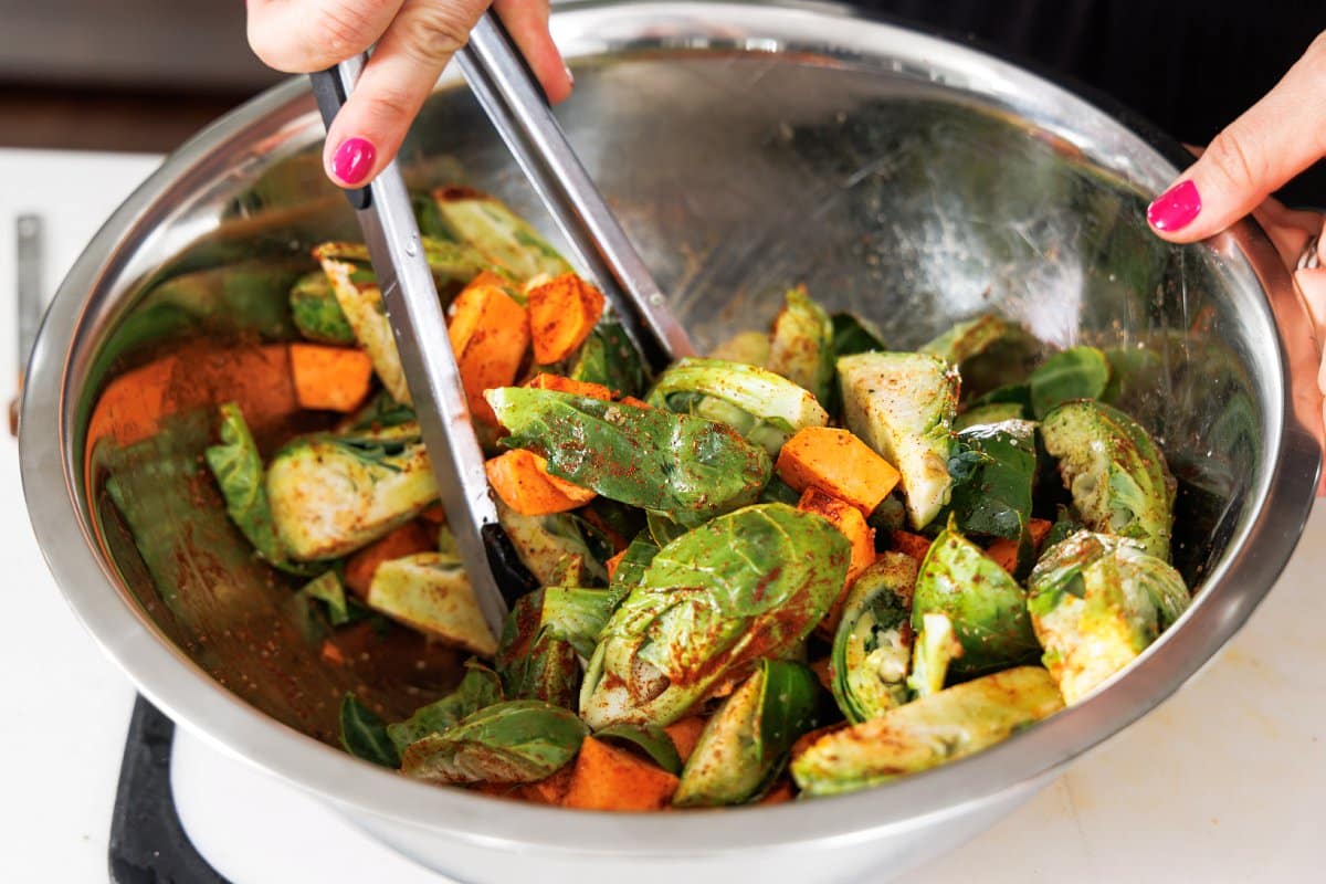 Tossing chopped veggies in seasoning in a large metal bowl.