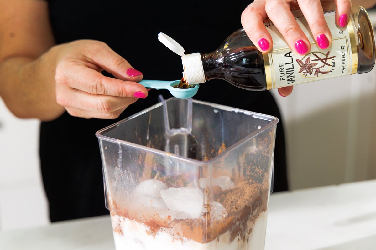 Adding vanilla extract to ingredients in a blender.