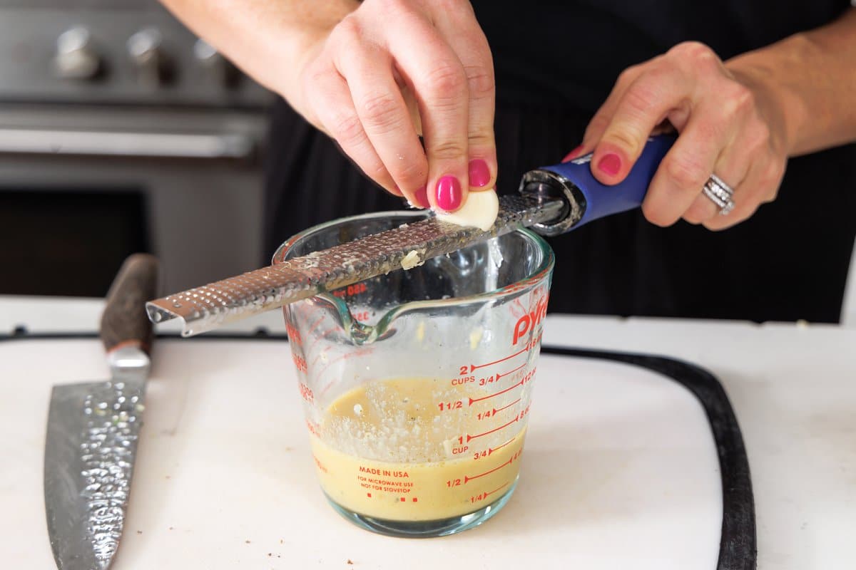 Using a microplane to grate a garlic clove into liquid measuring cup.