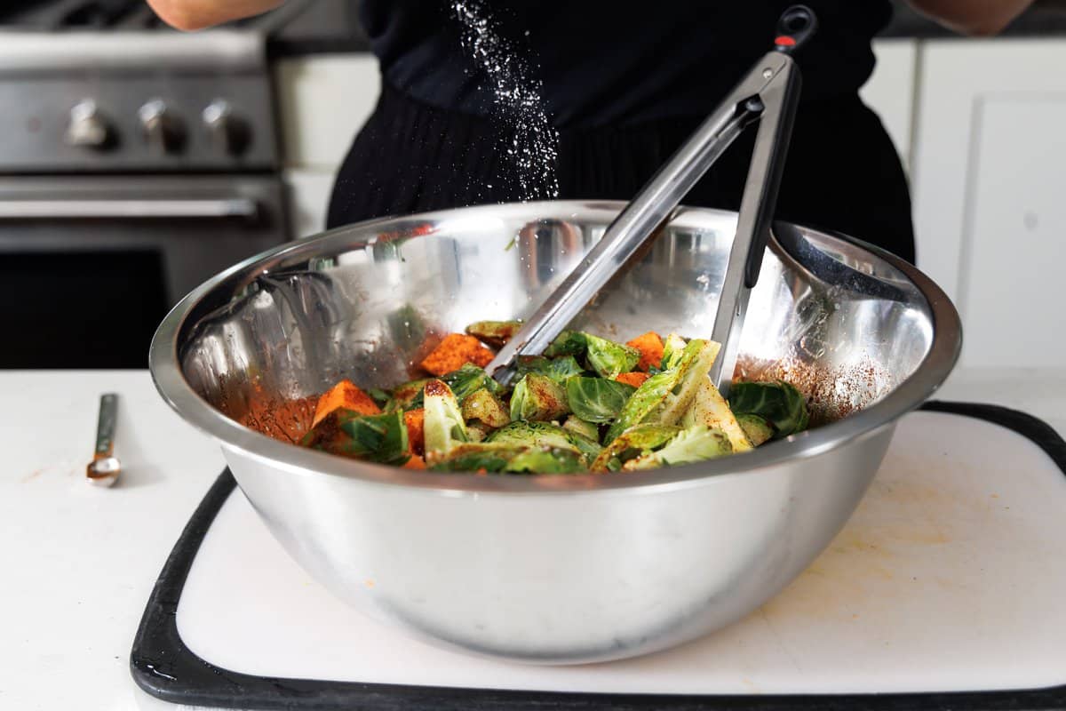 Sprinkling salt onto chopped veggies in a large metal bowl.