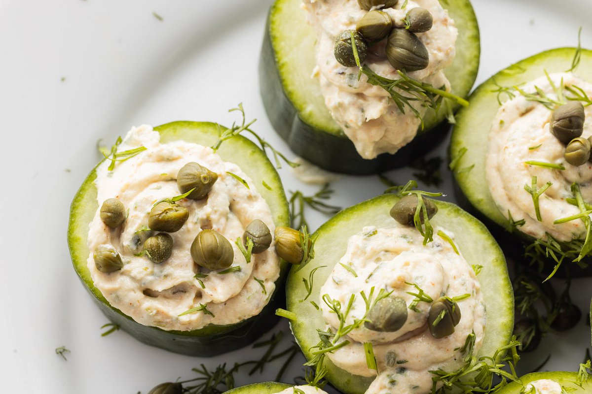 Close up of smoked salmon spread on cucumber rounds with dapers and dill.