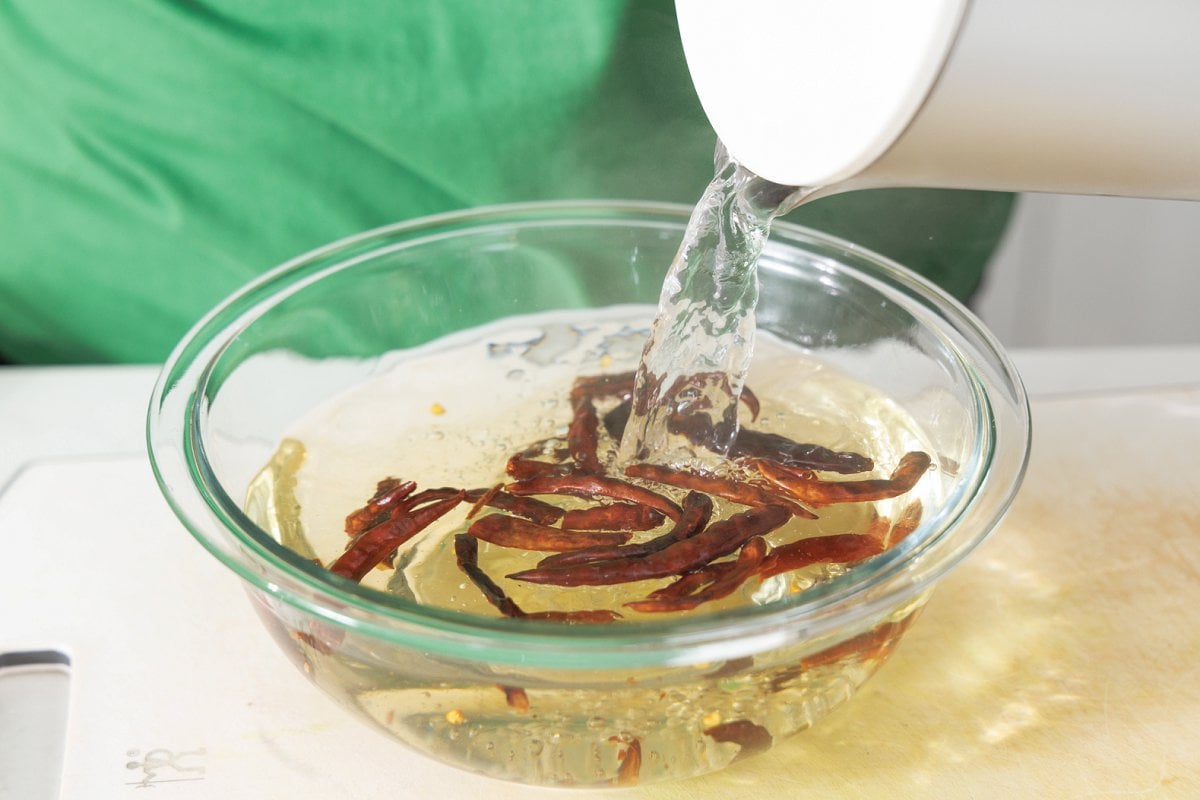 Rehydrating dried chiles in a glass bowl with hot water.