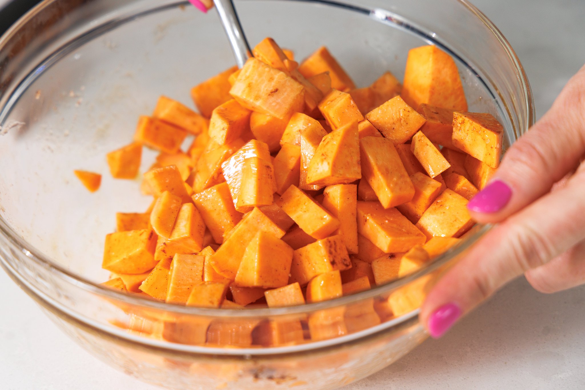 Tossing sweet potatoes in cinnamon, oil, and maple syrup.