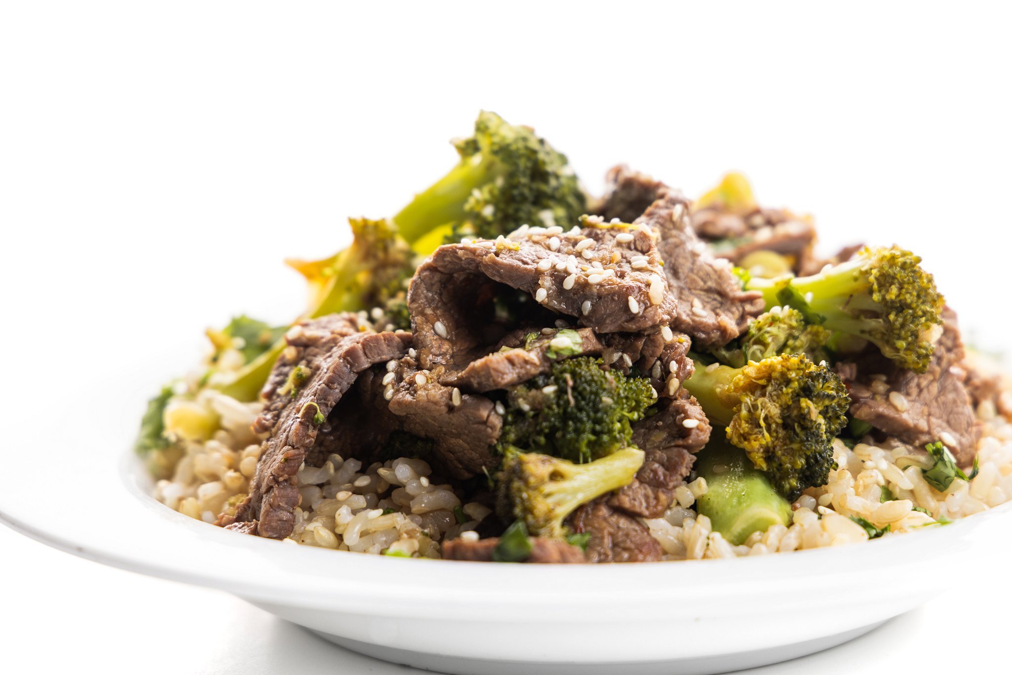 Plate full of brown rice topped with beef and broccoli.