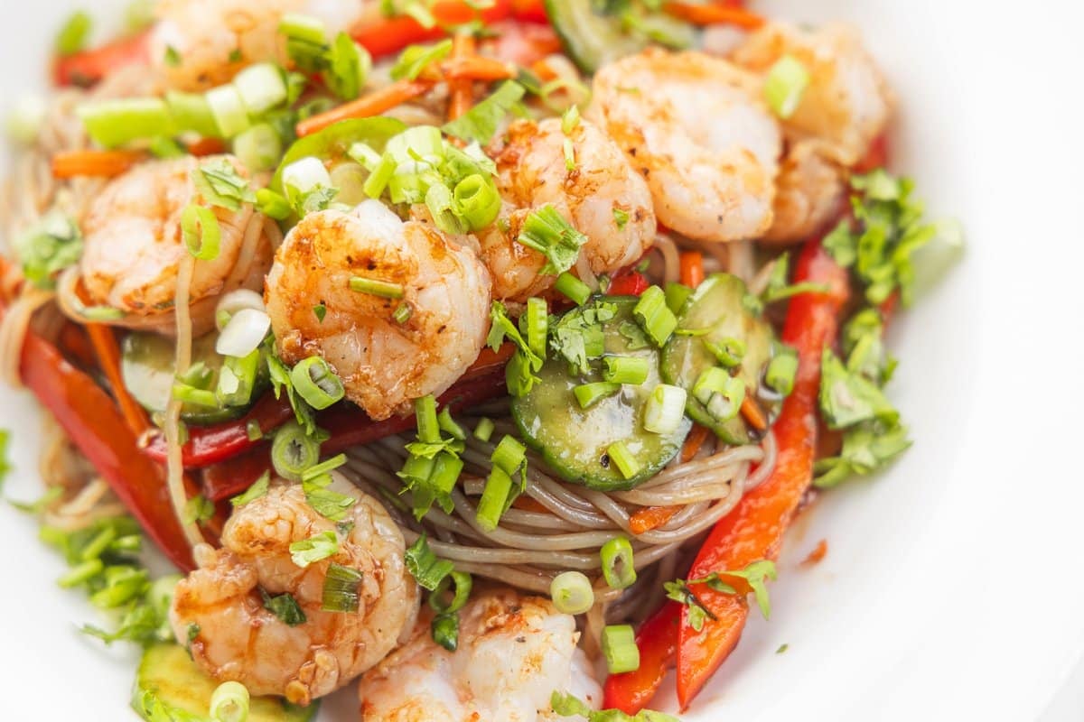 Thai shrimp salad with rice noodles topped with minced scallions on a white plate.