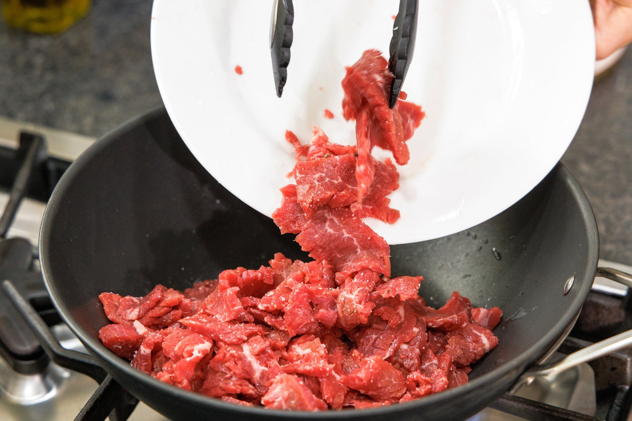 Adding beef strips to wok.