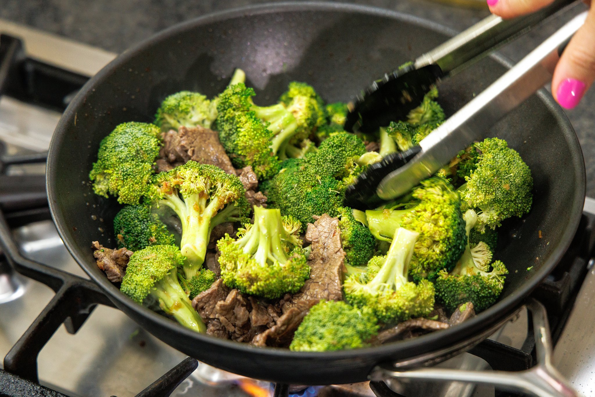 Tossing fresh broccoli florets in wok with cooked beef.