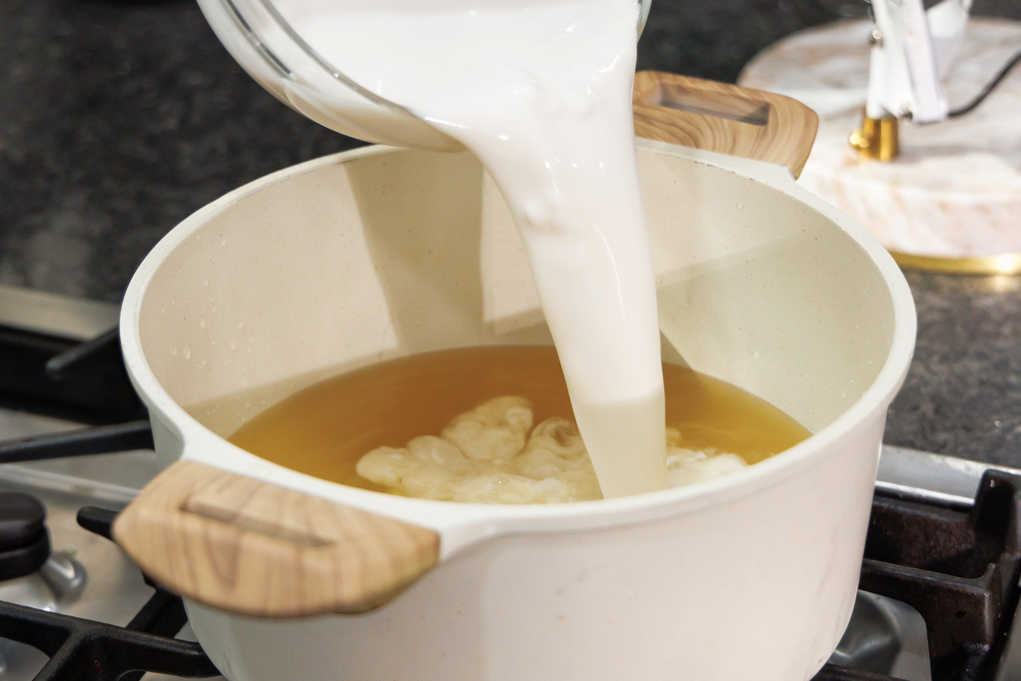 Pouring coconut milk into pot with chicken broth.