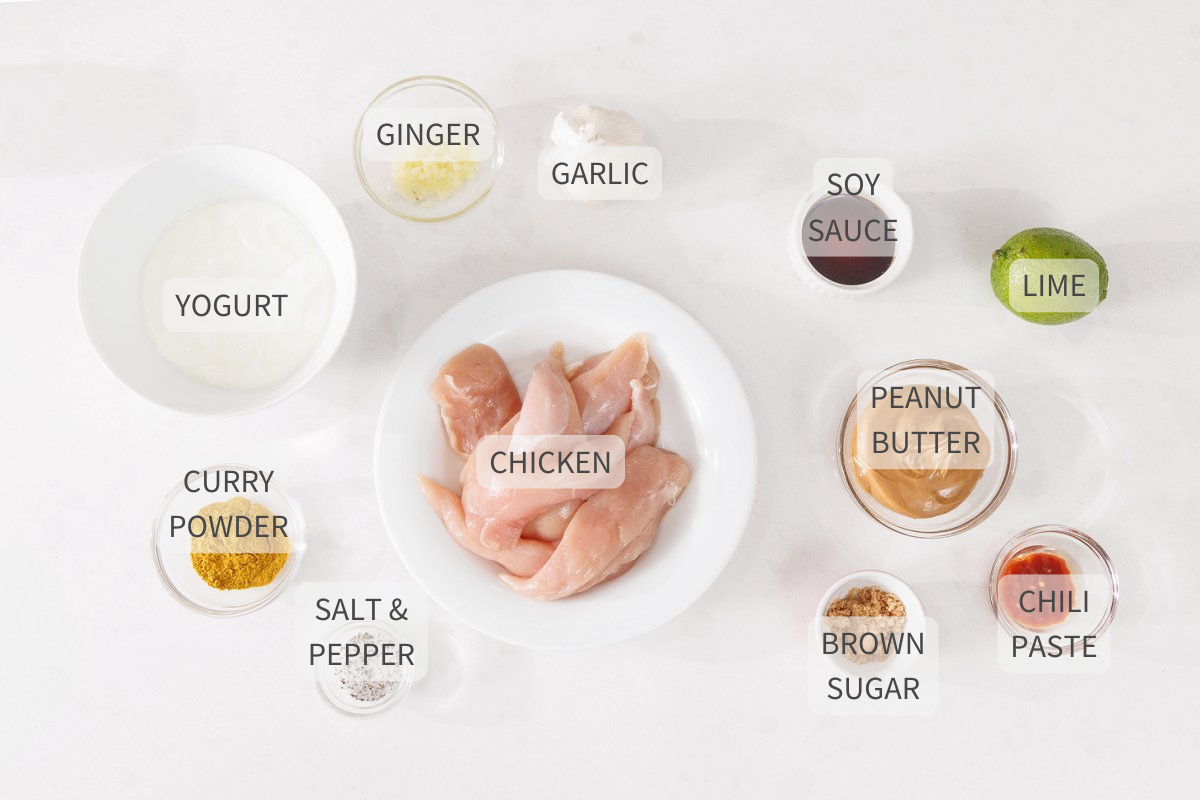 Labeled ingredients for chicken satay with peanut sauce on a white counter.