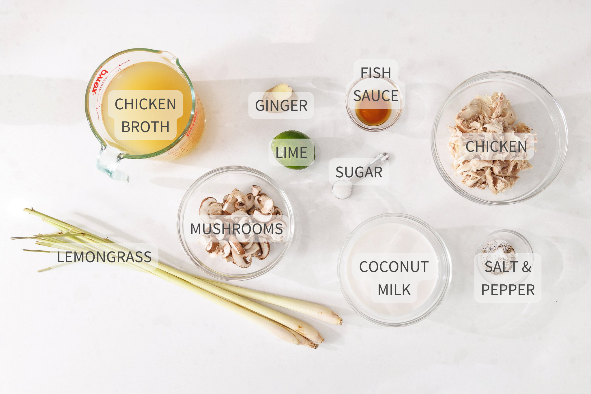 Labeled ingredients for tom kha gai soup on a white counter.