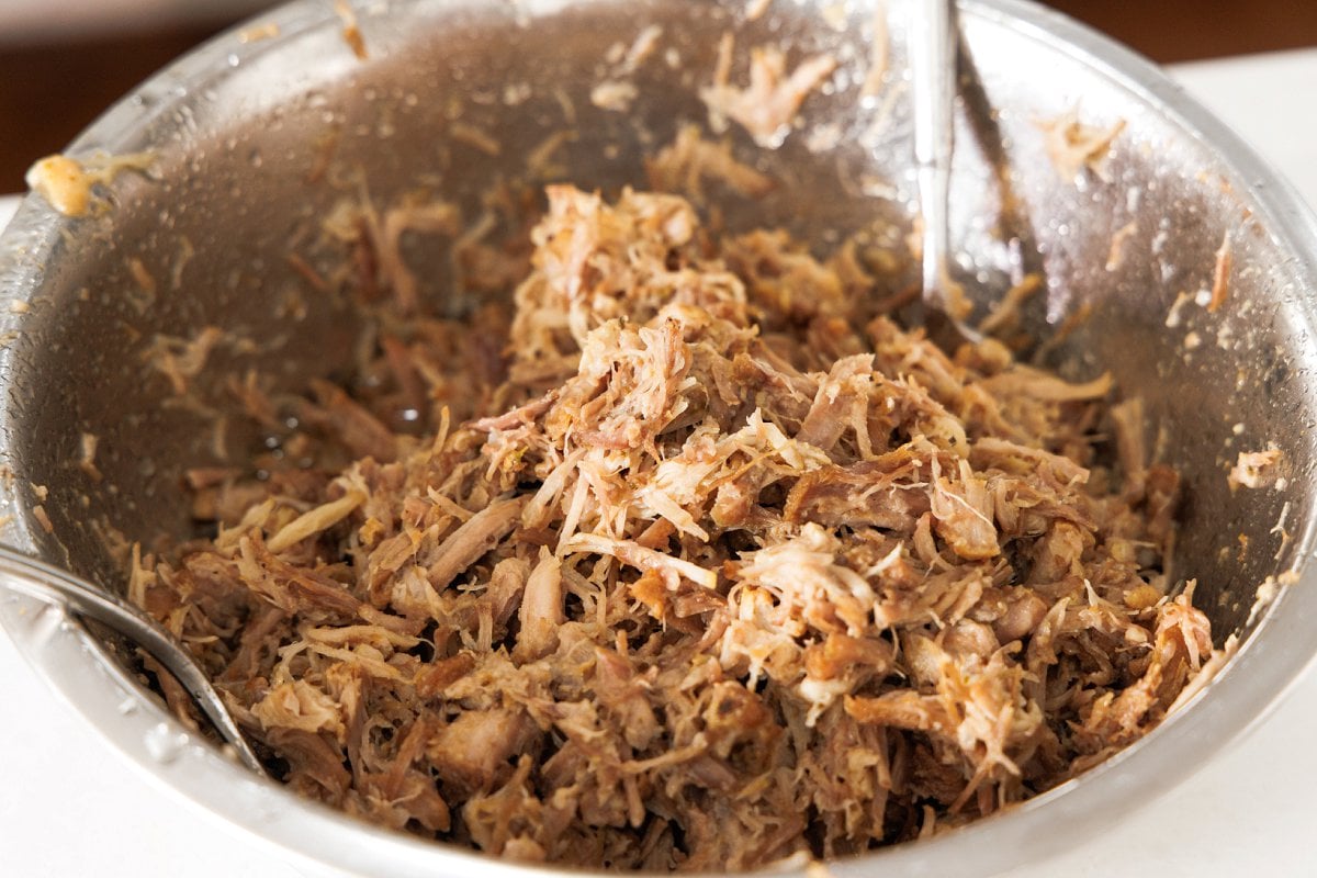 Shredded pork carnitas in a large metal bowl.