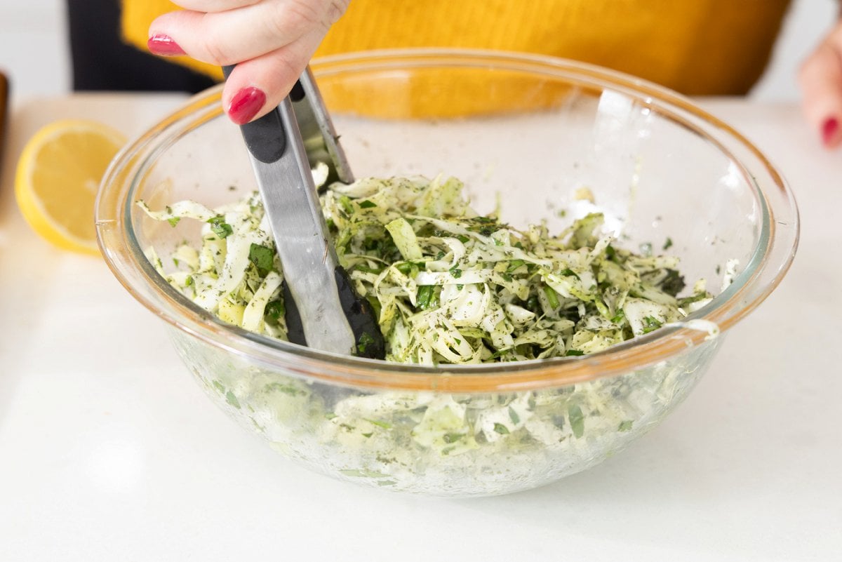Tossing Lebanese cabbage salad in dressing and seasonin.