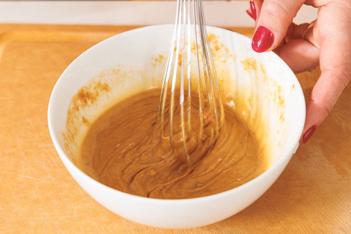 Whisking together peanut sauce in a white bowl.